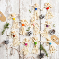 Decorative angel figures with colourful accents on a wooden surface with pine cones and ribbons.