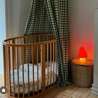 Wooden crib with checkered curtain and red mushroon night light in a room.
