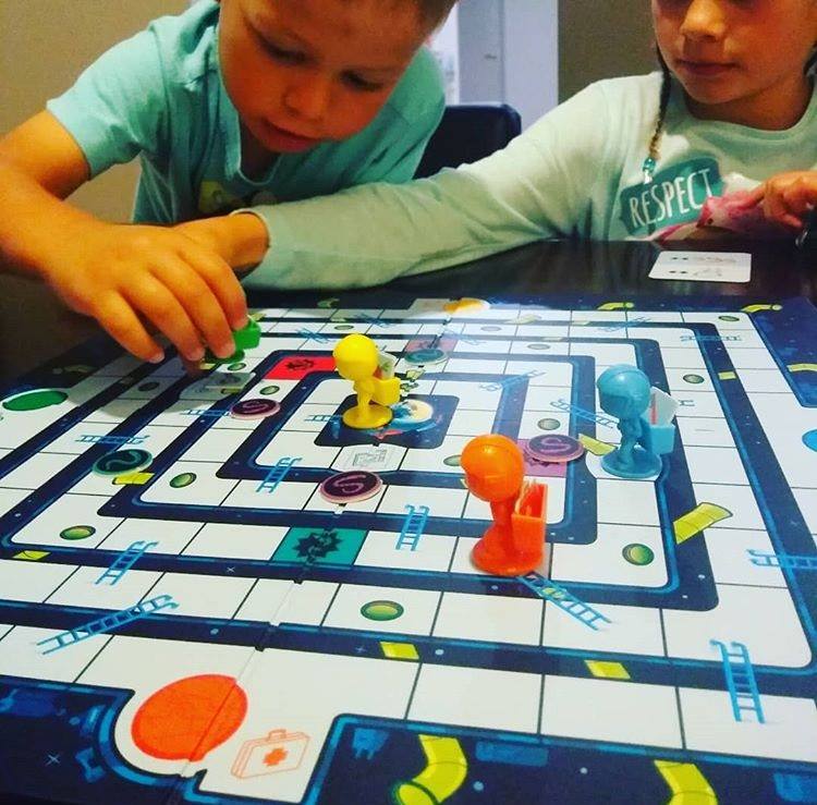 Two children playing a board game with colorful game pieces on a table.